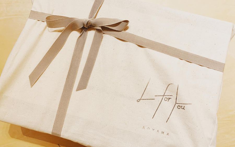 生成りの布で包み、細いリボンを結んだ贈りもの。布には L for You AOYAMA のロゴが入っている