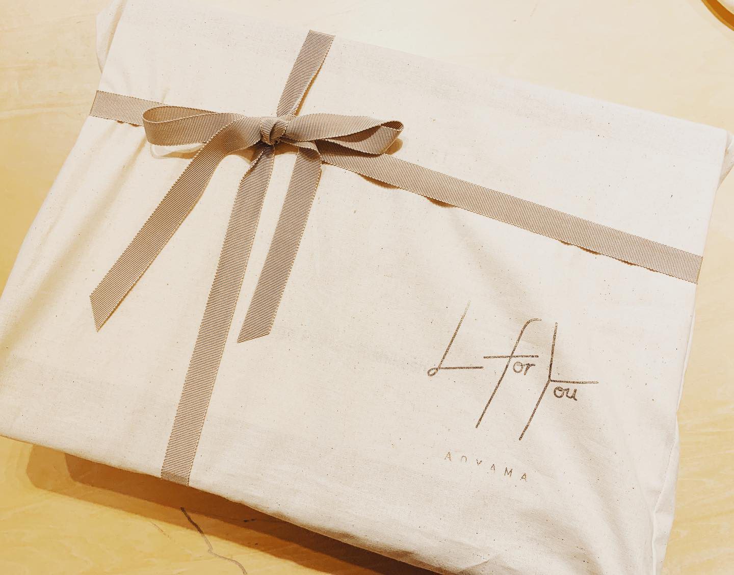 L for You AOYAMA のロゴが入った生成りの布張りのギフトボックス。同系色のリボンを十字に結んでいる