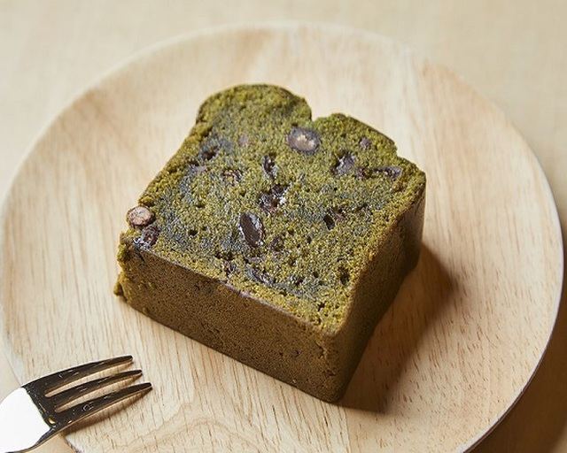 木の皿にのせた、小豆の粒が入った緑色のクロレラの米粉パウンドケーキ